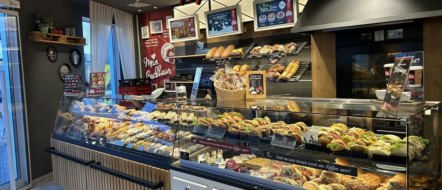 baeckerei-musswessels-Leer-Ceka.jpg Verkaufstheke mit frischen Brötchen, belegten Snacks und Gebäck in moderner Bäckereieinrichtung.