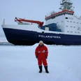 Jennifer_Dannheim-eigenes Foto.JPG Person in roter Kälteschutzkleidung steht auf Eisfläche vor dem Forschungsschiff Polarstern.
