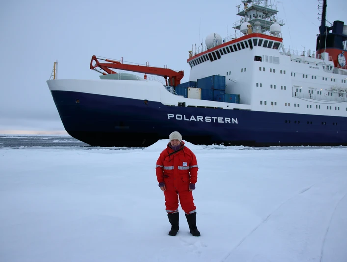 Jennifer_Dannheim-eigenes Foto.JPG Person in roter Kälteschutzkleidung steht auf Eisfläche vor dem Forschungsschiff Polarstern.