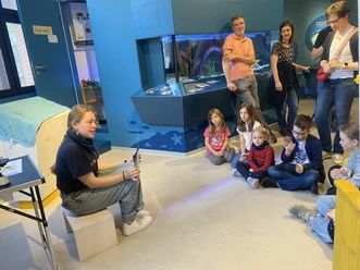 Nordseestunde im Nationalpark-Haus Eine Gruppe von Kindern hört einer Mitarbeiterin im Nationalpark-Haus bei einer Meerestierführung zu.