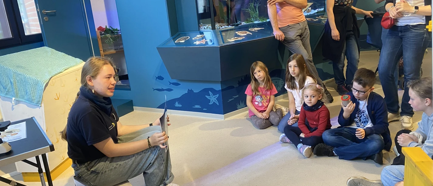 Nordseestunde im Nationalpark-Haus Eine Gruppe von Kindern hört einer Mitarbeiterin im Nationalpark-Haus bei einer Meerestierführung zu.