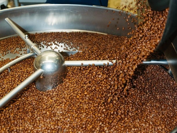 Röstereibesichtigung bei Van Dyck Frische Kaffeebohnen fallen aus der Röstmaschine in eine große Kühltrommel