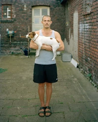 Alexander Lackmann: Ulvi, from the series "Ganz ehrlich", 2022 A man holds a small dog in the courtyard between old brick walls
