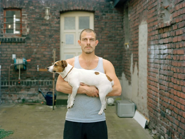 Alexander Lackmann: Ulvi, from the series "Ganz ehrlich", 2022 A man holds a small dog in the courtyard between old brick walls