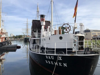 Rau IX IMG_3009 (c) Mailin Knoke_Erlebnis Bremerhaven_WEB.jpg Schlepper Rau IX im Museumshafen Bremerhaven mit deutscher Flagge am Heck und ruhigem Wasser.
