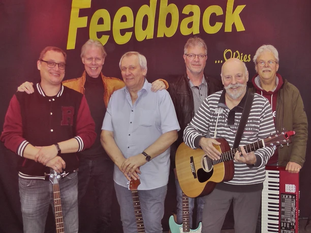 Feedback.JPG Sechs Männer stehen vor einer Wand mit dem Schriftzug 'Feedback', zwei halten Gitarren, einer steht vor einem Keyboard.