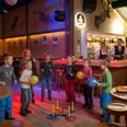 Fröhliche Tanzstimmung an der Kinderbar Fröhliche Kinder tanzen bei der Kinderdisco im Hotel Alpfrieden mit Ballons vor einer rustikalen Holzbar.Cheerful children dance with balloons in front of a rustic wooden bar at the children's disco in the Hotel Alpfrieden.Des enfants joyeux dansent avec des ballons devant un bar en bois rustique lors de la disco pour enfants à l'hôtel Alpfrieden.