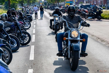 Motorräder bei Börjes_Heino Fecht.jpg Motorradfahrer auf einer belebten Straße beim Herbsttreff in Augustfehn, umgeben von geparkten Bikes.