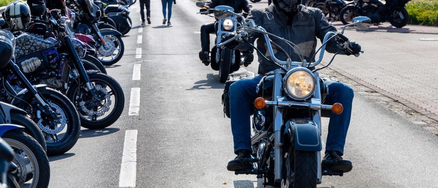 Motorräder bei Börjes_Heino Fecht.jpg Motorradfahrer auf einer belebten Straße beim Herbsttreff in Augustfehn, umgeben von geparkten Bikes.