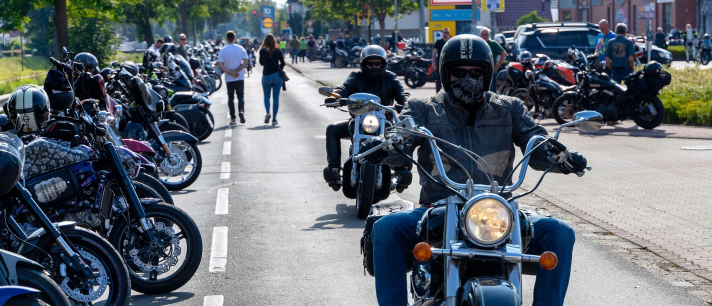 Motorcyklister på en trafikeret gade under efterårstræffet i Augustfehn, omgivet af parkerede motorcykler.
