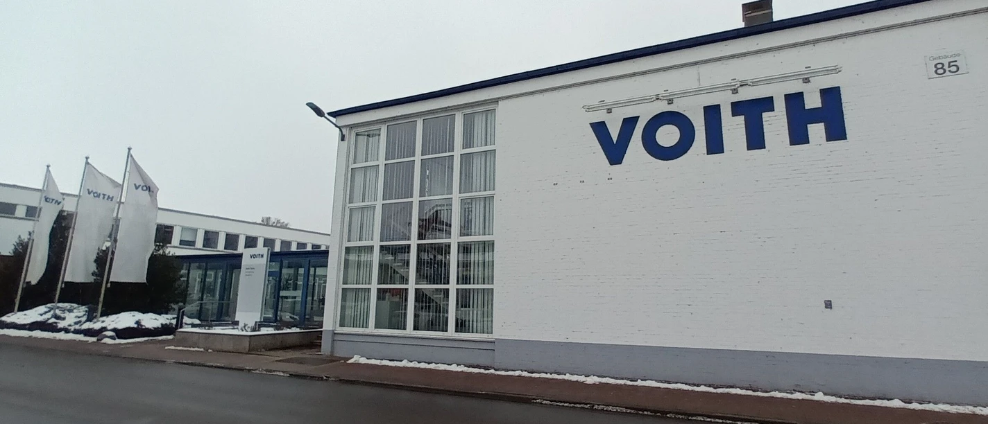 2026_Betriebsbesichtigung_Voith (2)_HD_16zu9.jpg Eingangsbereich des Voith-Werks in Salzgitter mit Firmenlogo und wehenden Fahnen an einem Wintertag