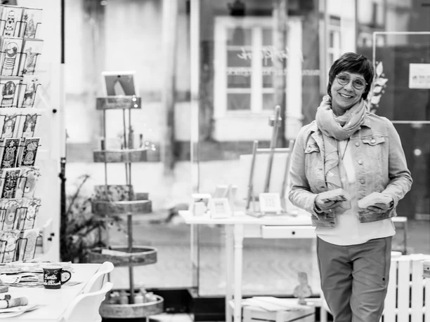 Schwarz-Weiß-Porträt einer lächelnden Frau im Kunstladen mit Kartenständer