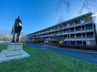 Parkhaus Lünepark Mehrstöckiges Parkhaus Lünepark unter blauem Himmel, davor eine dunkle Reiterstatue auf Rasen.