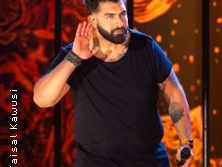 Ein Mann auf einer bunt beleuchteten Bühne hebt die Hand ans Ohr und hält ein Mikrofon.