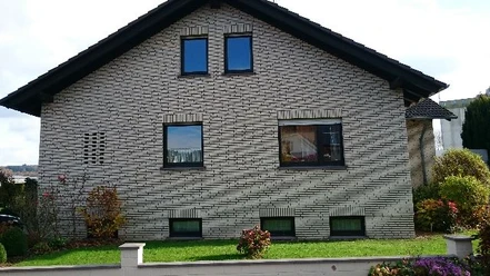 Helles Einfamilienhaus mit Klinkerfassade, Satteldach, mehreren Fenstern und Vorgarten.
