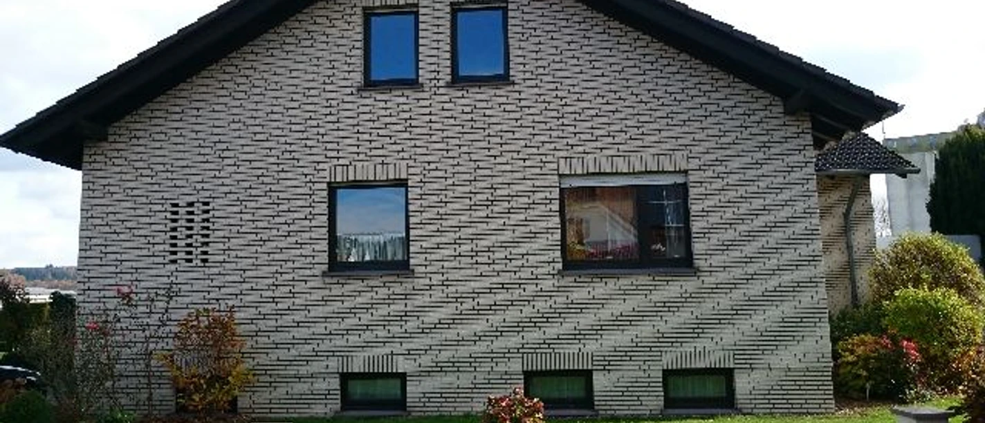 Ferienwohnung Tillmann-Hille Helles Einfamilienhaus mit Klinkerfassade, Satteldach, mehreren Fenstern und Vorgarten.