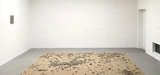Galerieraum mit Bodeninstallation aus Steinen auf Papier und kleinem Bild an der Wand