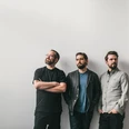Pablo Held Trio (c) Nancy Ebert.jpg Drei junge Männer in lässiger Kleidung stehen entspannt an eine weiße Wand gelehnt und schauen in verschiedene Richtungen.