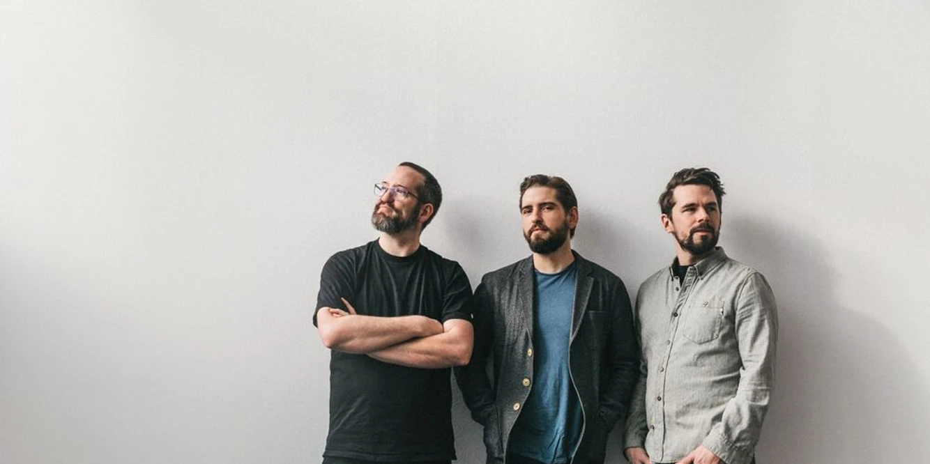 Pablo Held Trio (c) Nancy Ebert.jpg Drei junge Männer in lässiger Kleidung stehen entspannt an eine weiße Wand gelehnt und schauen in verschiedene Richtungen.