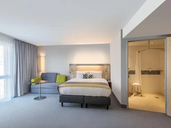 Holiday Inn Express Gütersloh Modernes Hotelzimmer mit Doppelbett, Sitzbereich, Tageslicht und offenem Bad