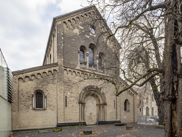 Brick building with Romanesque arches next to a glass façade and bare trees in the courtyard.