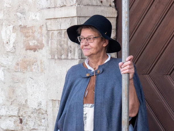 WF-Nachtwächterin.jpg Ältere Frau trägt Umhang und Hut. Sie hält eine Hellebarde vor einer alten Tür.