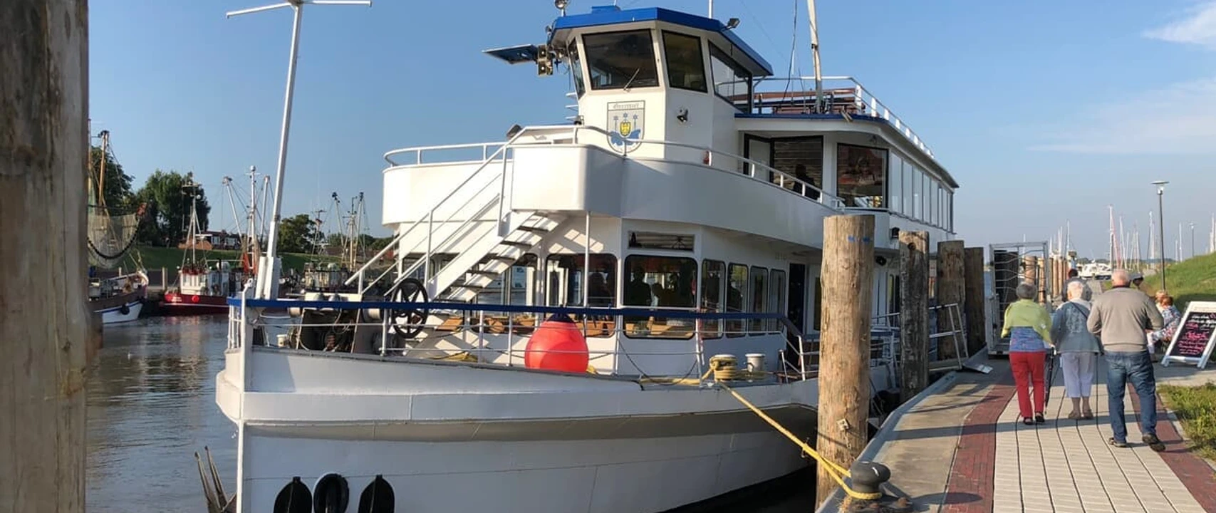 Fahrgastschiff Graf Edzard Weißes Fahrgastschiff mit blauem Dach liegt im Hafen von Greetsiel, Passagiere gehen an Bord.