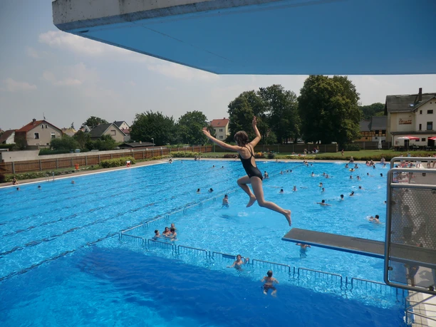 A child courageously jumps into the cool water from the 3-meter tower in the Naunhof forest pool.