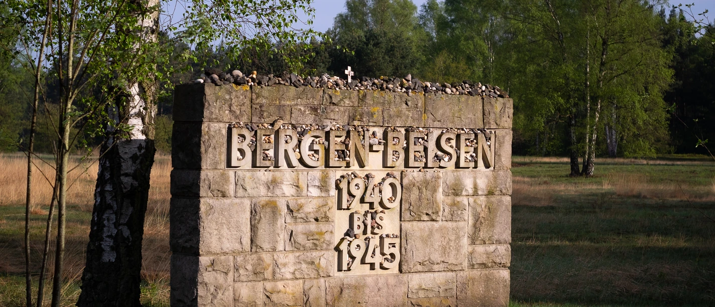 20180427-Bergen-Belsen-032-Bein.jpg Steinerne Gedenktafel mit Inschrift „Bergen-Belsen 1940 bis 1945“ in ruhiger Landschaft