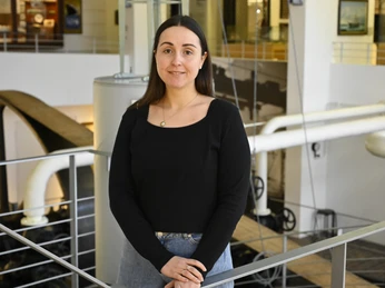 Maja_Dreyer_(c)AstridOttens.JPG Person mit dunklem Oberteil steht in moderner Innenhalle mit Rohren und Geländern.