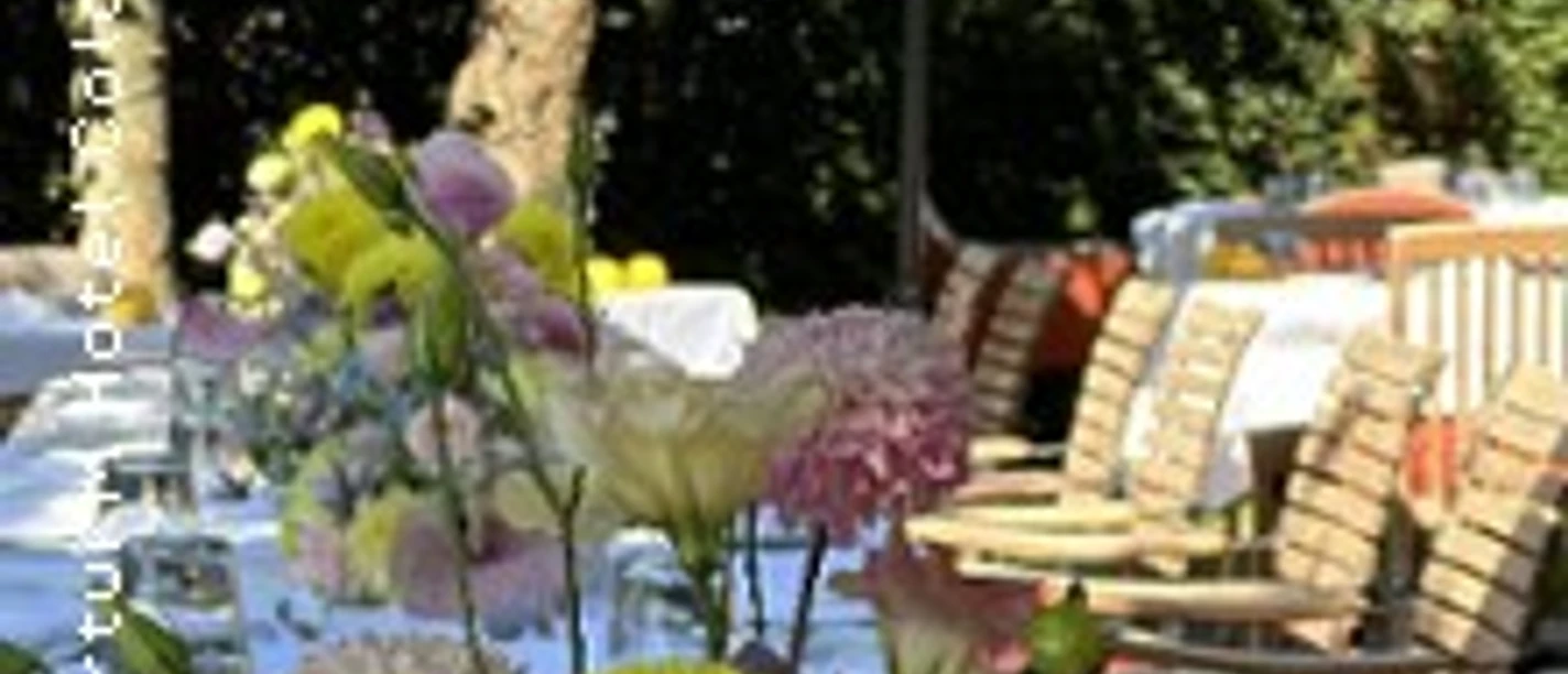 Blumengesteck auf gedeckter Terrasse mit Sonnenschirmen und Sitzplätzen im Grünen