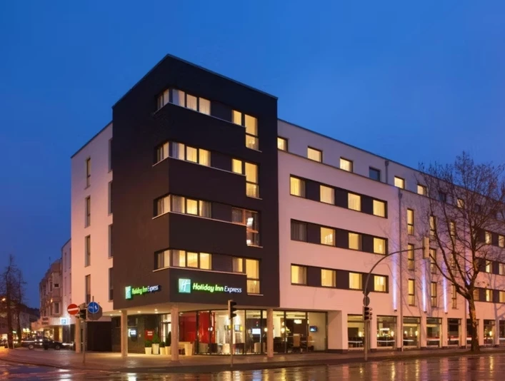 Holiday Inn Express Gütersloh Modernes Holiday Inn Express Hotel in Gütersloh bei Dämmerung, Eckgebäude mit beleuchteten Fenstern