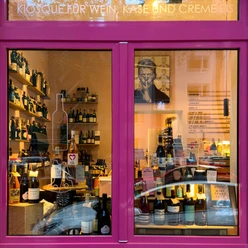 wine&glory Kiosque & Eisdiele Pink gerahmtes Schaufenster mit dicht arrangierten Weinflaschen und Regalen im Innenraum