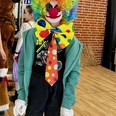 Clown beim Kinderkarneval in Apen 2025_Jörg Brandes.jpg Bunt verkleideter Clown mit Regenbogenperücke, roter Nase und großer Schleife in der Turnhalle.