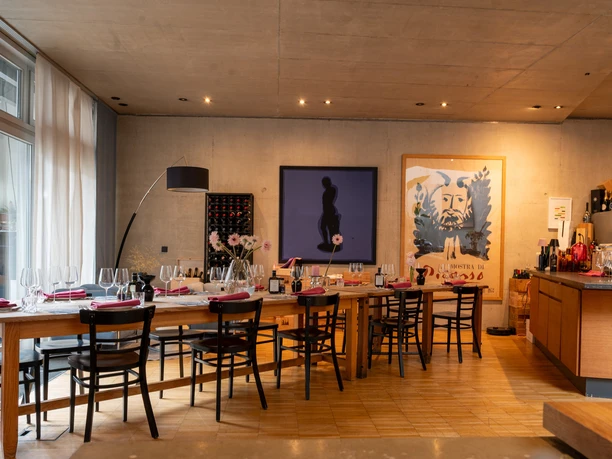 wine&glory Location Modern room with a long wooden table, art on a concrete wall and a wine bottle rack.