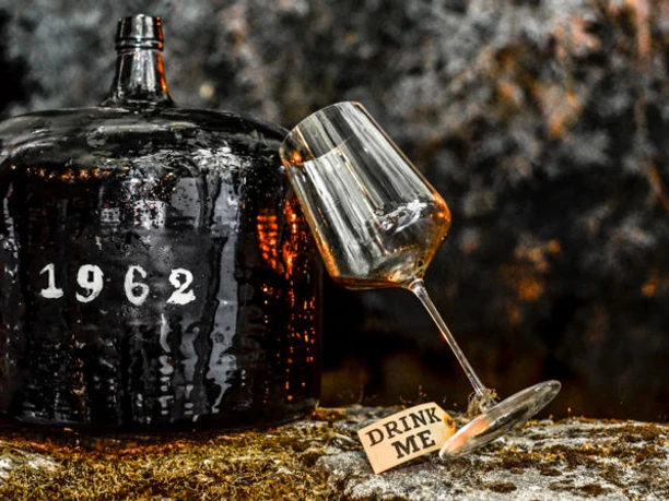 Red wine seminar Old wine demijohn with inscription 1962 next to slanted glass and sign Drink Me