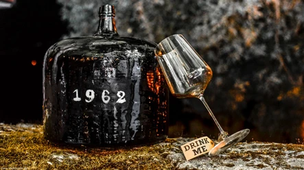 Rotweinseminar Alter Weindemijohn mit Aufschrift 1962 neben schrägem Glas und Schild Drink Me