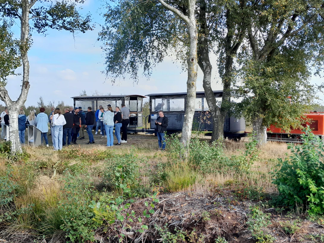 Moorbahn im Uchter Moor.jpg Besuchergruppe steht im Moor neben offener Lorenbahn, umgeben von Birken und Heidegras.