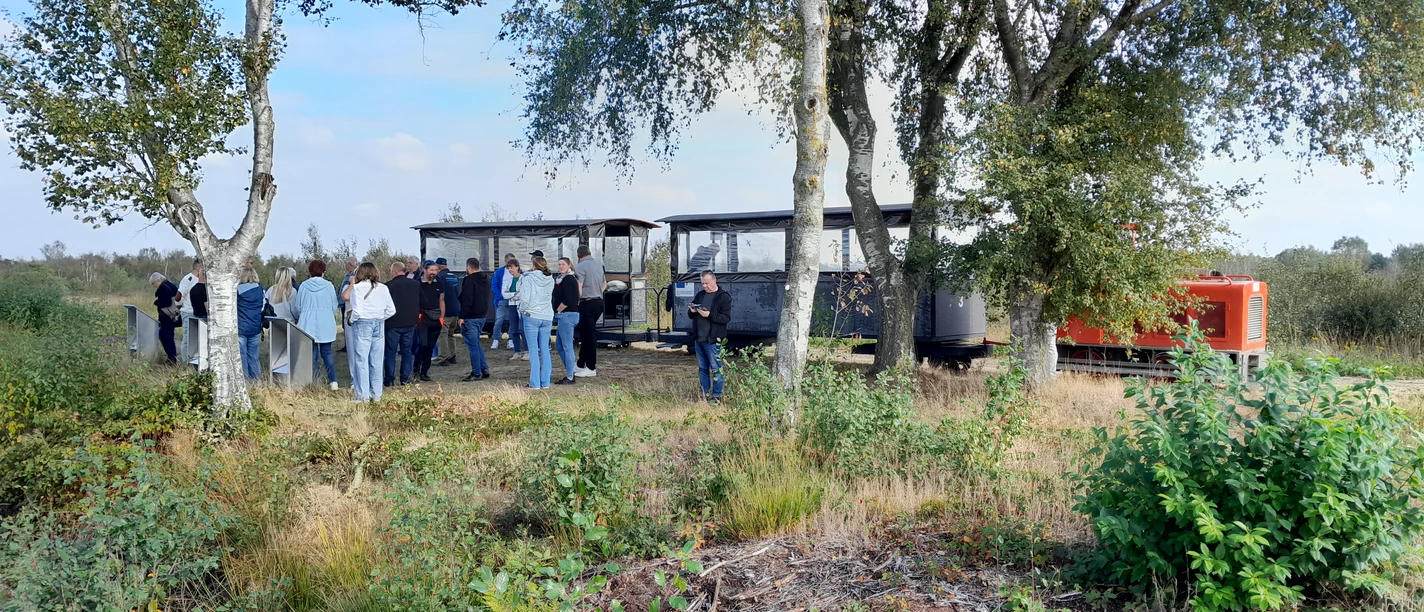 Moorbahn im Uchter Moor.jpg Besuchergruppe steht im Moor neben offener Lorenbahn, umgeben von Birken und Heidegras.