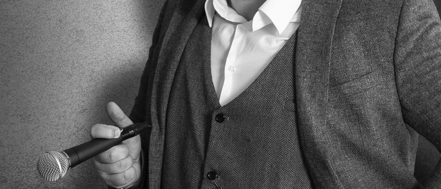 Jan Philipp Zymny Porträt von Jan Philipp Zymny in Anzug, mit Mikrofon und Pistole in der Tasche, in Schwarz-Weiß.