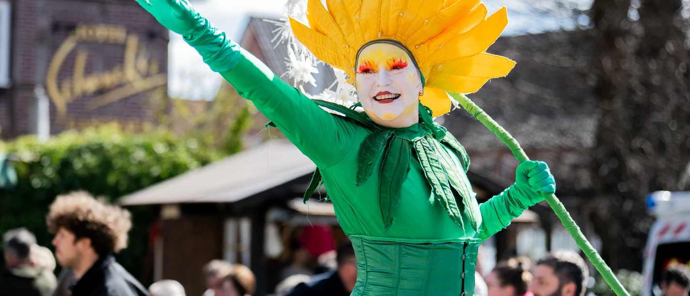 shotz-7120.jpg Bunter Walkact als Löwenzahn verkleidet winkt fröhlich auf dem Frühlingsmarkt in Amelinghausen.
