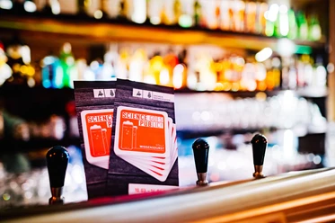 Flyer der Veranstaltungsreihe Science Goes Public auf einer Bar mit Zapfhähnen und Flaschen