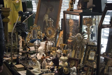 Antikmarkt & Design.jpg Antikmarktstand mit religiösen Objekten, Leuchtern, Figuren, Büchern und Glasvitrinen.