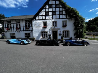 Fachwerkfassade des Schlosshotels Gimborn mit drei Oldtimern unter blauem Himmel