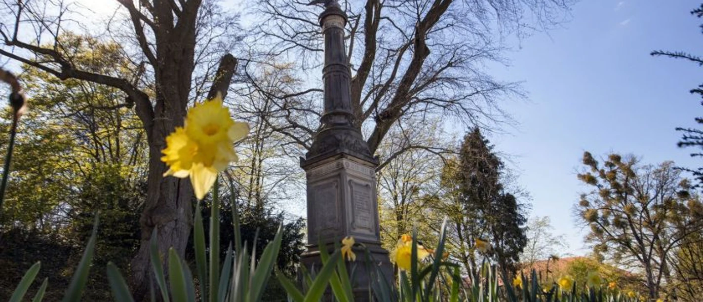 Denkmal Denkmal mit Säule und Adlerfigur, davor blühende Narzissen im Park