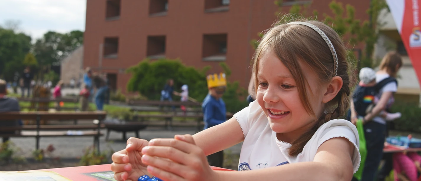 maedchen-spieltisch-1920x1280.jpg Ein Mädchen spielt mit Würfeln an einen Spieltisch im Garten