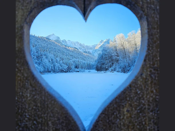 Blick auf den Riessersee Verschneiter See und Berge durch ein herzförmiges Fenster in winterlicher Landschaft.