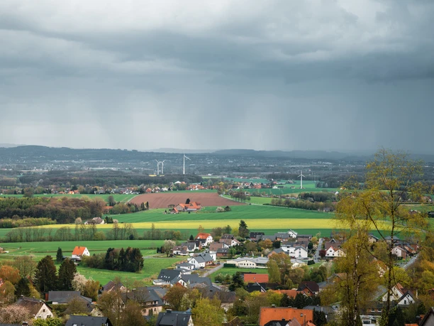 Blick über Dorf, Felder und Windräder unter dunklen Regenwolken