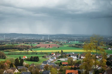 Wiehengebirge Blick über Dorf, Felder und Windräder unter dunklen Regenwolken