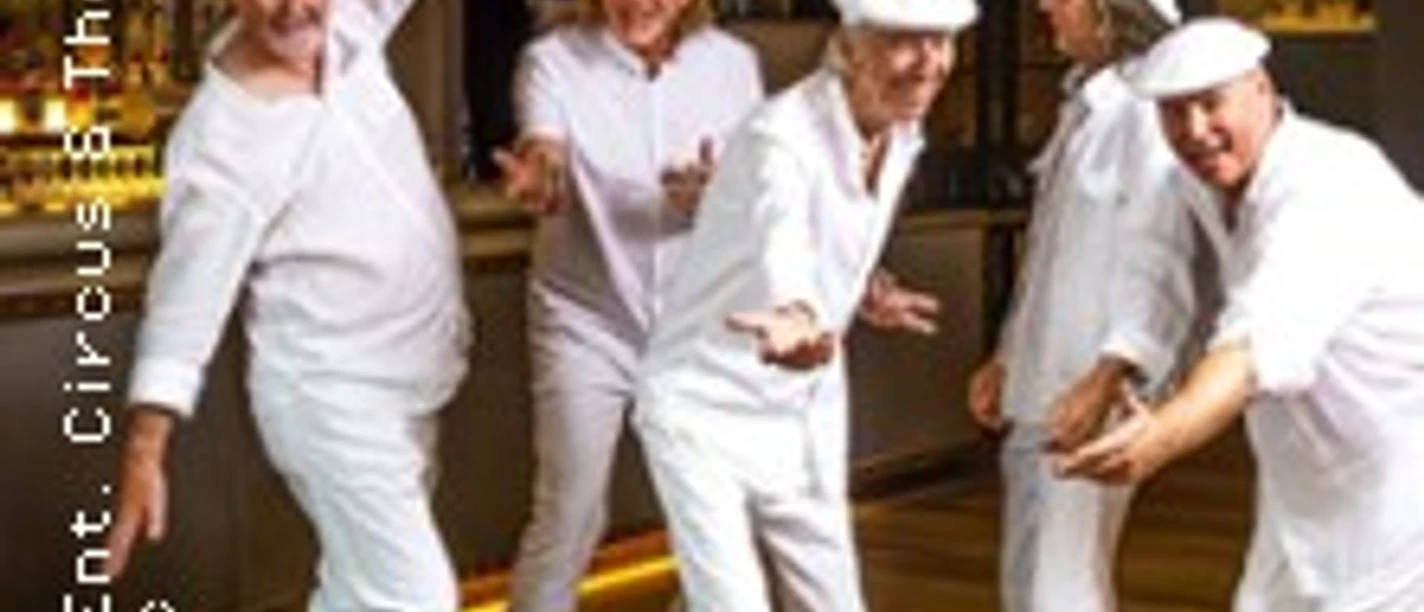 Fünf in Weiß gekleidete Personen posieren tanzend in einem hellen Raum mit warmem Licht